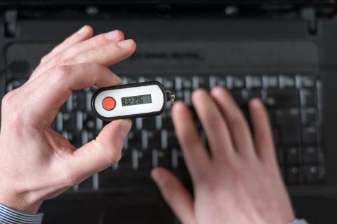 Man holding a RSA token above a notebook and entering the token code with the second hand to log in.