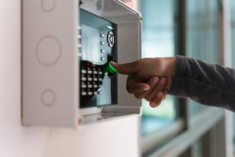 Person logs into a biometric access system by fingerprint that hangs on a wall.