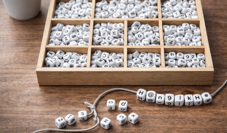 Inside a wooden box are beads, each bearing a different letter, number, and special character; in front of it is a string on which some beads have already been strung to form a password.