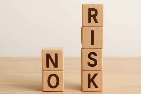 Letters are written on wooden cubes stacked in two towers on a table, forming the words NO RISK.